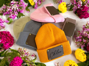Personalised baby beanies in pink, yellow, beige, grey and brown with vegan leather name patches.