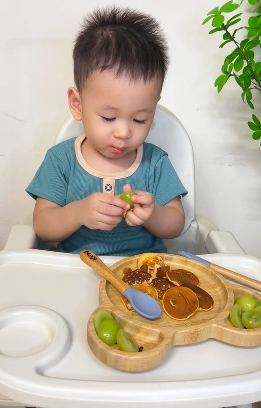 A toddler using Bamboo table ware plate with food on it