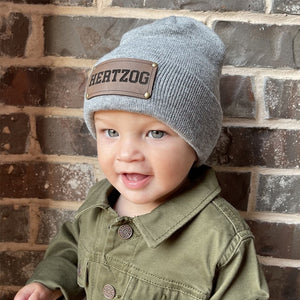 Child wearing a gray beanie with 'HEATZOG' logo against a brick wall