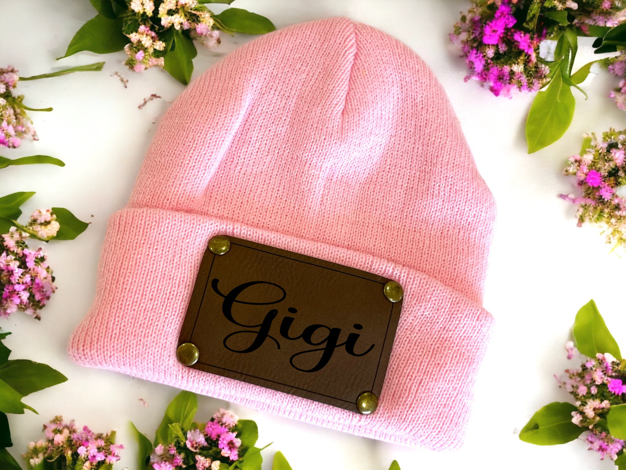 Pink personalised baby beanie with vegan leather name patch surrounded by flowers.