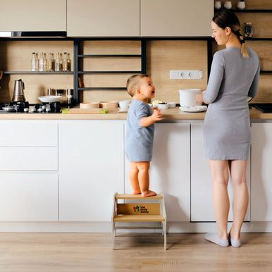 A baby using step stool to learn cooking with parents