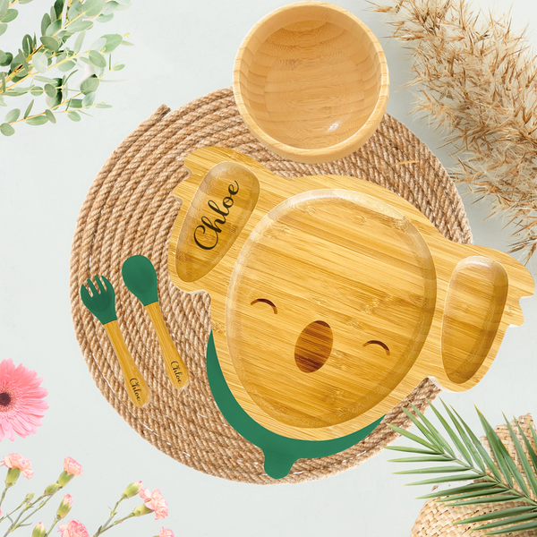 Personalized bamboo koala-shaped toddler plate with the name 'Chloe' engraved, featuring separate food compartments. Includes a matching bamboo bowl and utensils with green silicone tips, all engraved with 'Chloe.' Perfect eco-friendly dining set for kids is Ideal for sustainable and custom baby products, promoting environmentally conscious parenting.