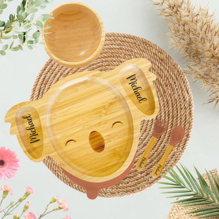 Customized bamboo koala-shaped plate for kids, engraved with the name 'Michael' on both ears, featuring compartments for food. Includes a matching bamboo bowl and utensils with brown silicone tips, also engraved with 'Michael.' this eco-friendly dining set is perfect for toddlers and environmentally conscious families.