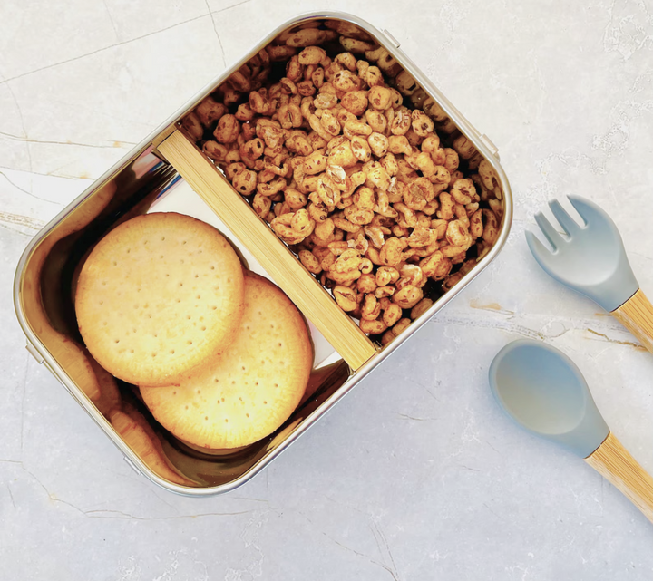 Open stainless steel personalised lunchbox with bamboo divider, filled with kids snacks like cereal and biscuits. Ideal for school or kindy meals